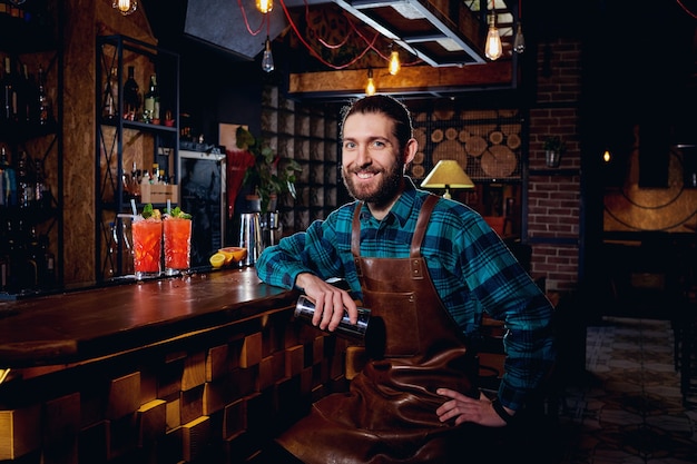 Retrato de un barman hipster con barba sonriendo sentado en la barra