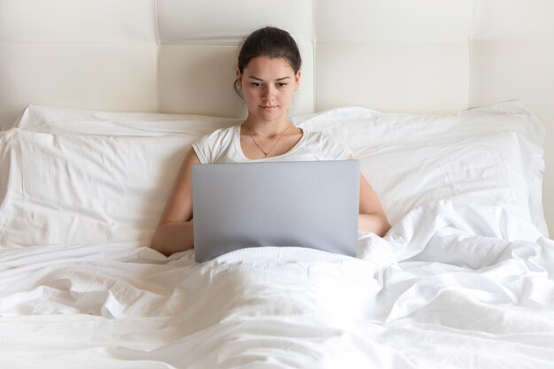 Retrato bastante joven con laptop en la cama por la mañana