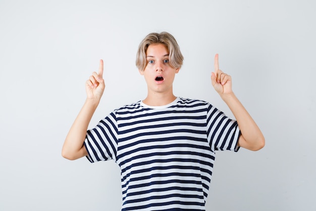 Retrato de bastante jovencito apuntando hacia arriba en camiseta a rayas y mirando sorprendido vista frontal