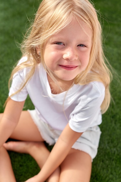 Foto retrato bastante sonriente chica rubia sentada sobre la hierba verde mock up camiseta blanca vista superior