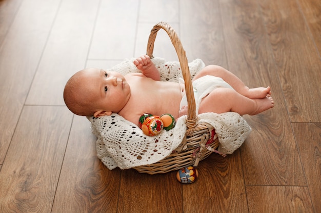 Retrato de un bebé lindo en la cesta de mimbre pascua. Pequeño bebé recién nacido en cesta de mimbre en la pared de madera. niño sonriente y huevos de pascua