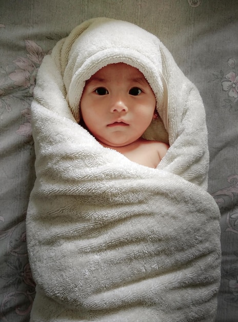Retrato de un bebé lindo envuelto en una toalla en la cama