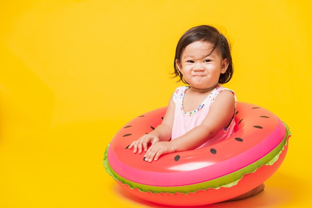 Retrato de bebé niña asiática usar traje de baño sentado en anillo inflable de sandía