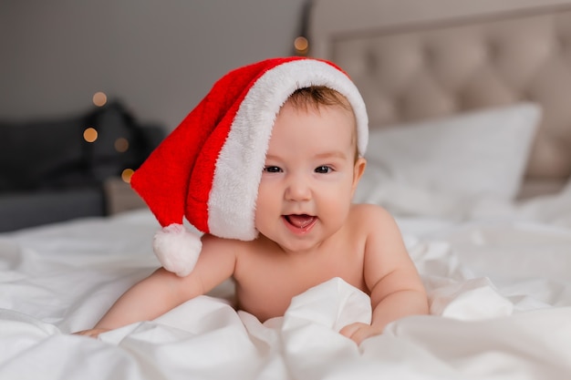 Retrato de un bebé en pañales y un gorro de Papá Noel acostado boca abajo sobre una sábana blanca