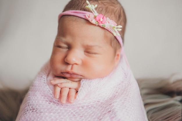 Retrato de un bebé recién nacido durmiendo en una diadema con flores. Concepto de salud: FIV, accesorios para bebés.