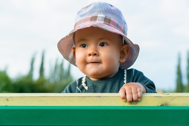 Retrato de un bebé recién nacido gordito en un sombrero de Panamá mirando desde detrás de un banco del parque