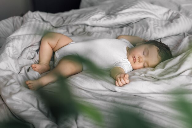 Retrato de bebé en ropa de dormir en la manta de la cama planta verde borrosa en primer plano Dormir boca arriba niño pequeño en el dormitorio ver dulce sueño Espacio de copia de enfoque suave Concepto de cuidado de niños y sueño saludable