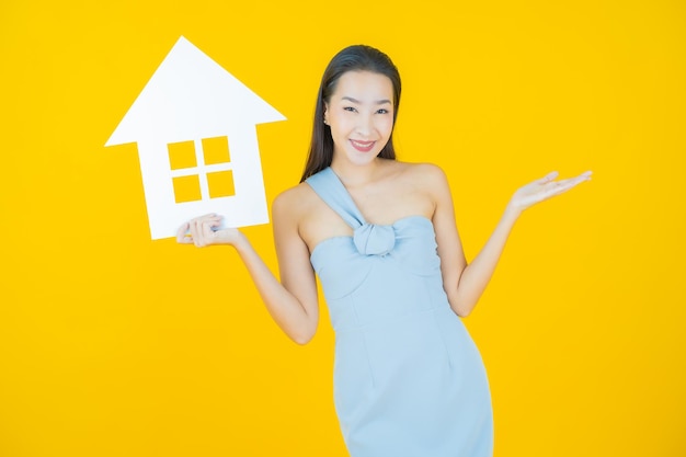 Retrato bela jovem asiática com casa ou sinal de papel em casa amarelo