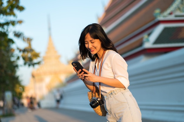 Retrato bela jovem asiática com telefone celular inteligente em torno da vista da rua ao ar livre em um dia de verão