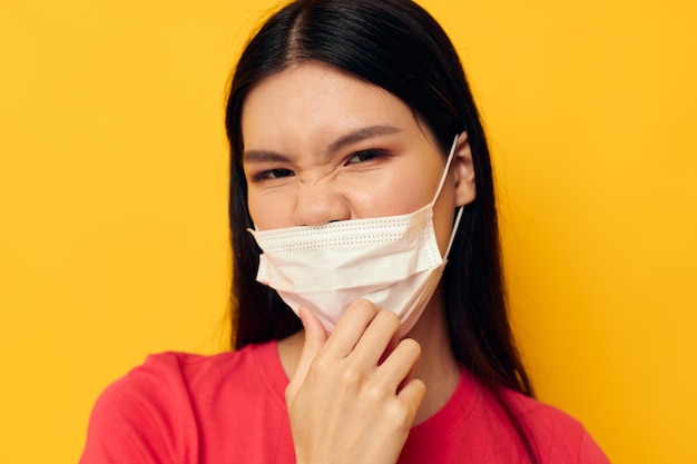 Retrato bela jovem asiática em camiseta vermelha proteção de máscara médica fundo amarelo inalterado