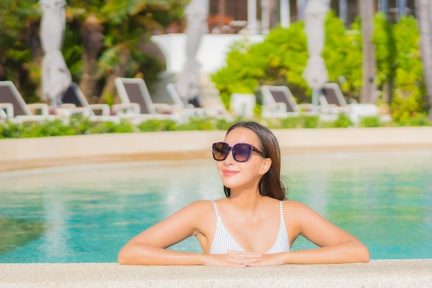 Retrato bela jovem asiática relaxando sorriso lazer ao redor da piscina ao ar livre com o mar oceano em viagens de férias