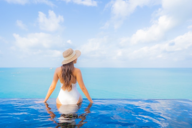 Retrato bela jovem asiática relaxando sorriso lazer ao redor da piscina ao ar livre com o mar oceano em viagens de férias