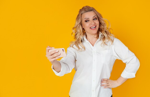 Retrato de una bella y bella mujer rubia caucásica sonriente tomando un selfie en un teléfono inteligente