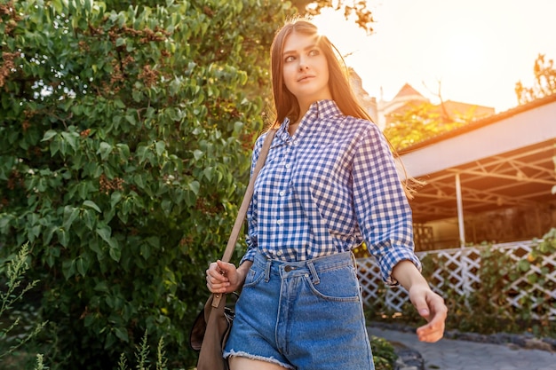 Retrato de una bella joven en las calles de la hermosa ciudad con follaje, arbustos, soleado día de verano.