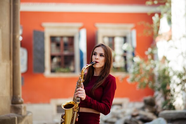 Retrato de una bella joven caminando por la calle con un saxofón