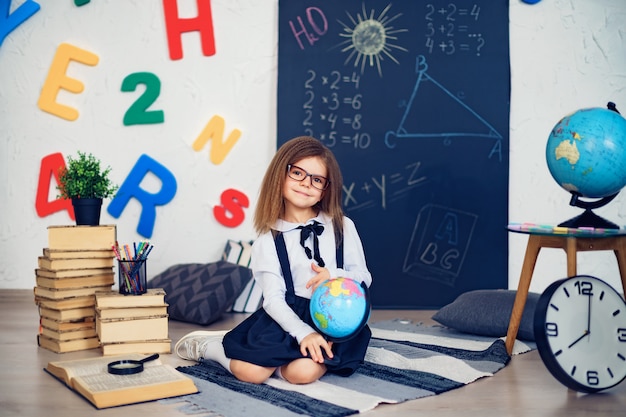 Retrato de una bella joven colegiala sosteniendo globo sentado en el suelo sobre la alfombra.