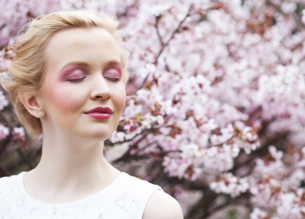 Retrato de una bella joven rubia sobre un fondo de flores de cerezo rosa en primavera