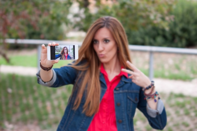 Retrato de una bella joven selfie en el parque con un teléfono inteligente