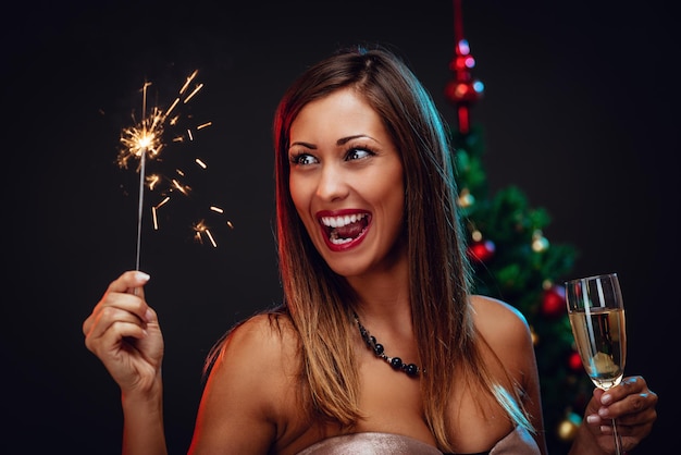 Retrato de una bella mujer alegre celebrando la Navidad. Ella se está divirtiendo con bengalas y champán.