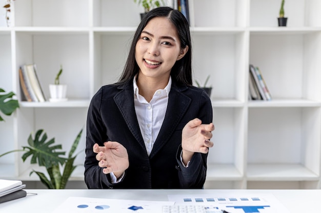 Retrato de una bella mujer asiática posando hablando con la cámara. Las mujeres de negocios jóvenes están levantando ambas manos como si estuvieran haciendo una videollamada con una persona. Concepto visual para videoconferencia.