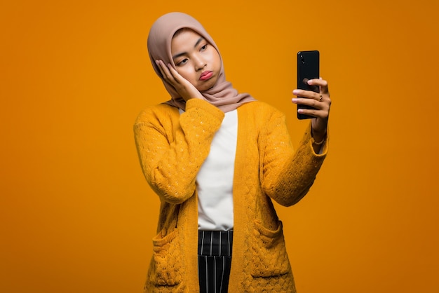 Retrato de una bella mujer asiática con un teléfono móvil con cara infeliz