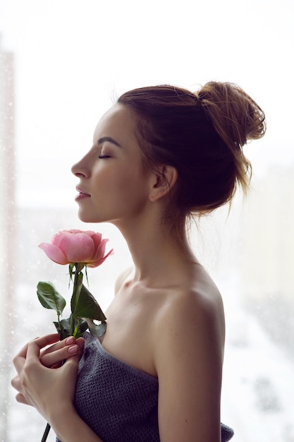 Retrato de una bella mujer atractiva en una toalla gris en el baño sosteniendo una rosa roja