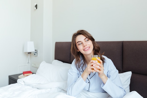 Retrato de una bella mujer bebiendo jugo de naranja en el dormitorio