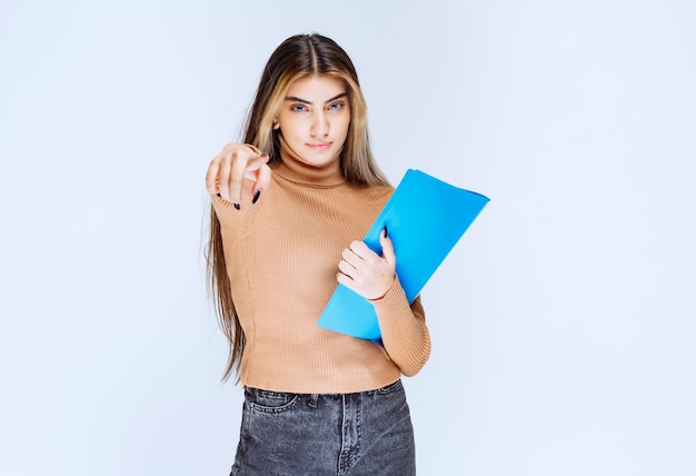 Retrato de una bella mujer con una carpeta de pie y apuntando a la cámara.