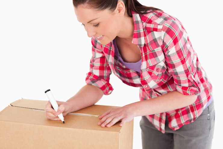 Foto retrato de una bella mujer escribiendo en cajas de cartón con un marcador mientras está de pie