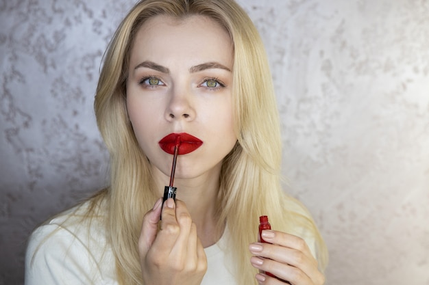 Retrato de una bella mujer joven que hace maquillaje con labios rojos brillantes