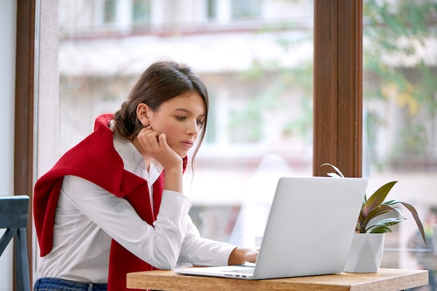 Retrato de una bella mujer joven sentada frente a su computadora portátil concentrándose