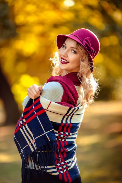 Retrato de una bella mujer joven con un sombrero burdeos en otoño en un paseo por el parque