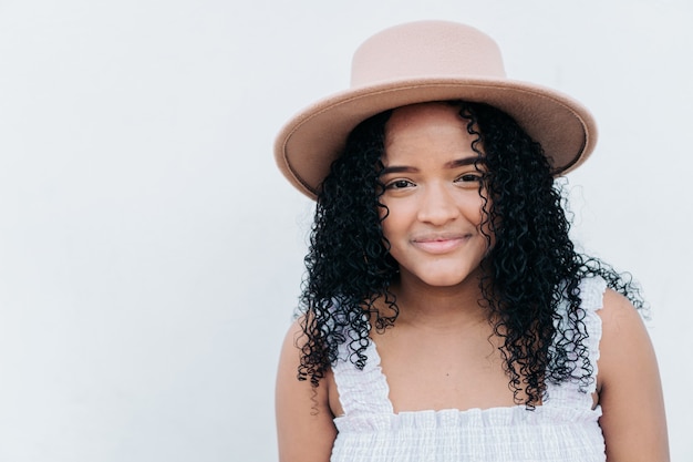 Retrato de una bella mujer joven con un sombrero en la calle de la ciudad sobre un fondo de pared blanca.