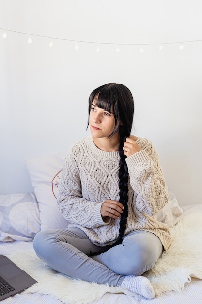 Retrato de una bella mujer joven sonriendo y haciendo una trenza en el pelo en traje de invierno en casa