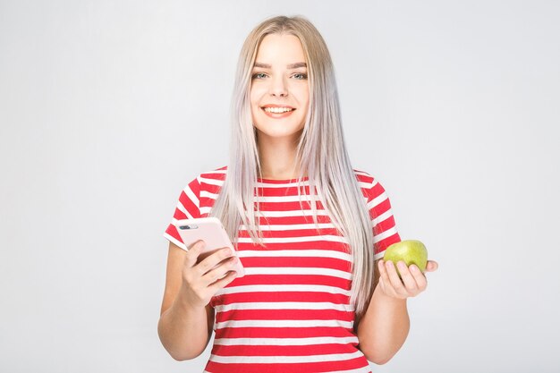 Retrato de una bella mujer joven sosteniendo una manzana y un teléfono sobre un fondo blanco.