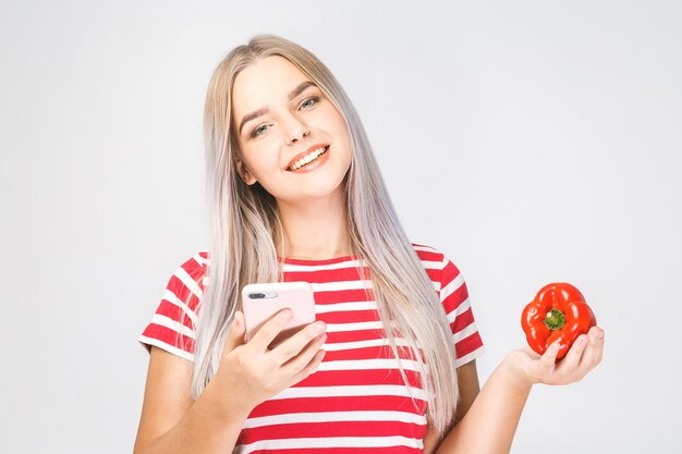 Retrato de una bella mujer joven sosteniendo un vegetal y teléfono sobre un fondo blanco.