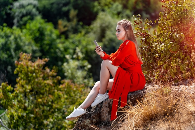 Retrato de una bella mujer joven en vestido rojo, naranja. Vista al parque Vista al lago borrosa de fondo. Pelo largo. Buen maquillaje Sesión de fotos profesional. De cerca.