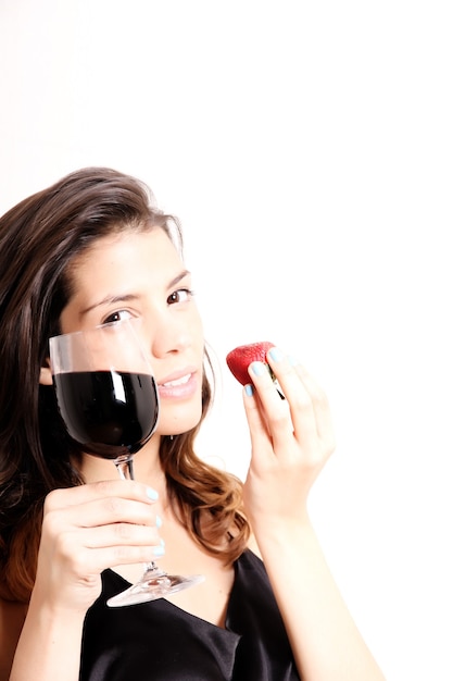 Retrato de una bella mujer latina comiendo una fresa y bebiendo vino.