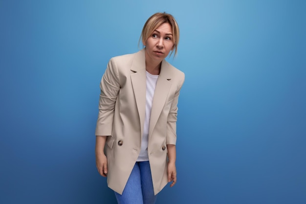 Retrato de una bella mujer milenaria rubia con una chaqueta color crema posando sobre un fondo azul