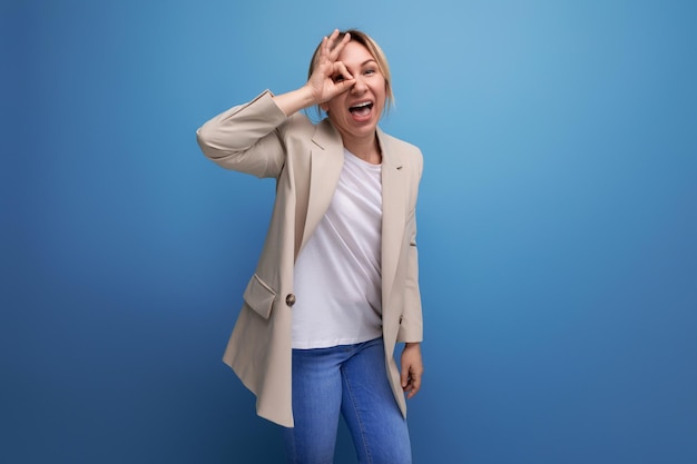 Retrato de una bella mujer milenaria rubia con una chaqueta color crema posando sobre un fondo azul