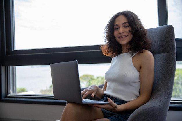 retrato de una bella mujer sonriendo, sentada en un sillón con su computadora