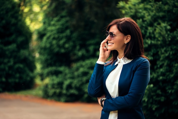 Un retrato de una bella mujer sonriente hablando por teléfono en el parque de la ciudad