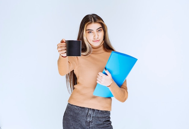 Retrato de una bella mujer sosteniendo una carpeta y ofreciendo una taza de bebida.