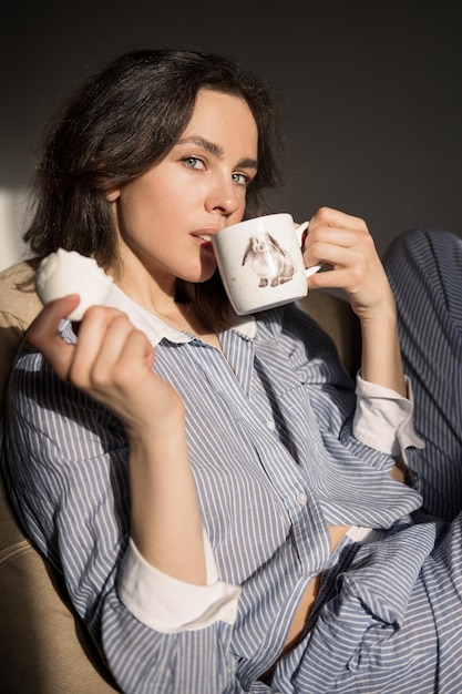 Retrato de una bella mujer vestida con pijama. Bebe café de una taza.