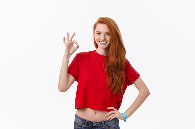 Retrato de una bella mujer en vestido rojo de santa claus mostrando signo bien y guiñando un ojo sobre blanco