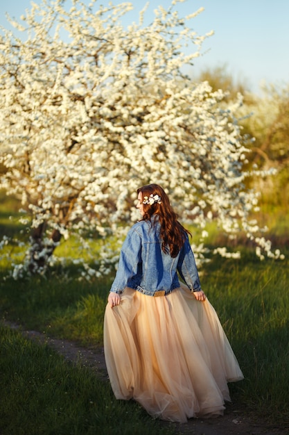 Retrato de una bella novia. Concepto de boda Boda elegante Gran luz del atardecer. Ella lleva una chaqueta de mezclilla azul, vestido. Jardín floreciente de primavera.