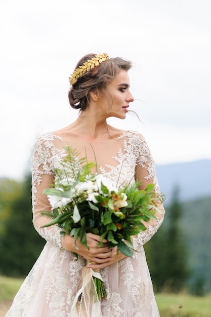 Retrato de una bella novia en las montañas. La niña sostiene un ramo de novia en sus manos.