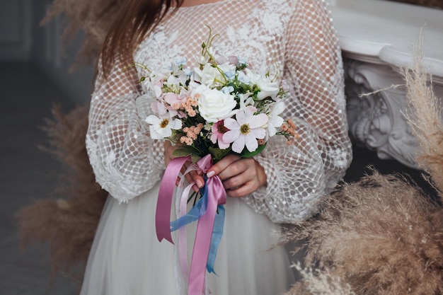 Foto retrato de una bella novia con un ramo de rosas blancas y margaritas rosas en las manos en un interior claro