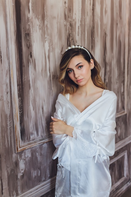 Foto retrato de una bella novia rubia en el interior. novia joven de la mañana en una bata de baño. fotografía de boda. niña sonriente y linda se encuentra.