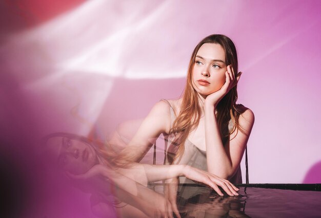 Foto retrato de belleza con agua de una joven modelo de moda con cabello largo y oscuro sobre un fondo rosa